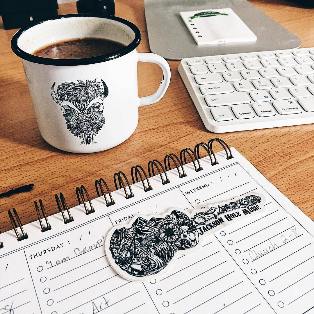 enamel mug with wolf design, keyboard, and planner on a wooden desk