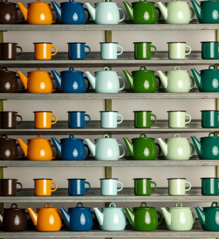 Shelves filled with colorful enamel teapots and enamel mugs on a metal shelf