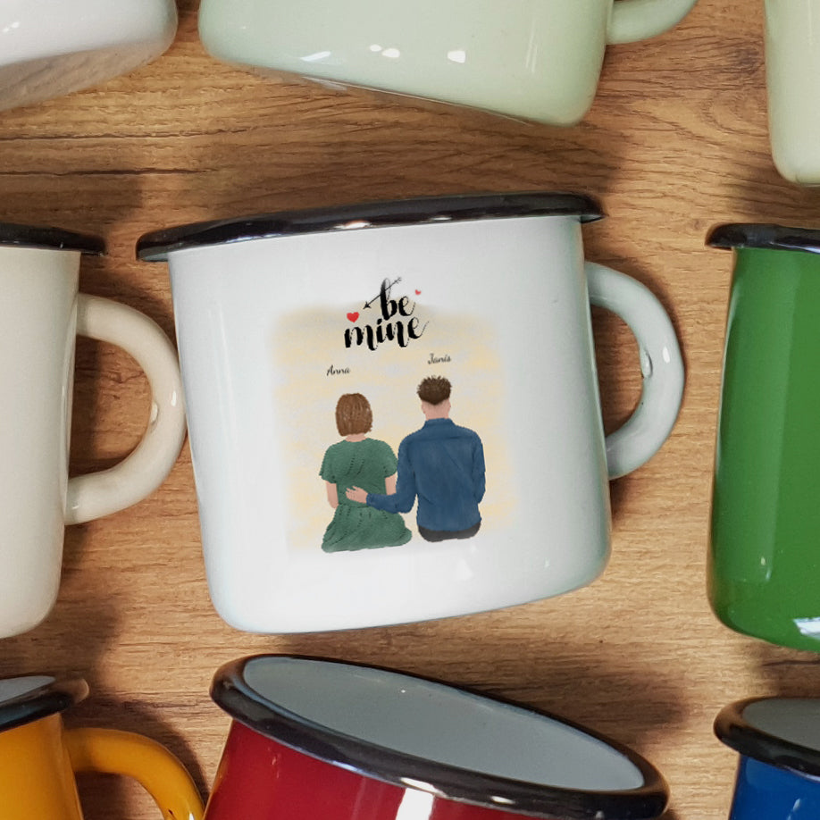 white enamel mug with a design of two people holding hands and 'be mine' text on a wooden surface.
