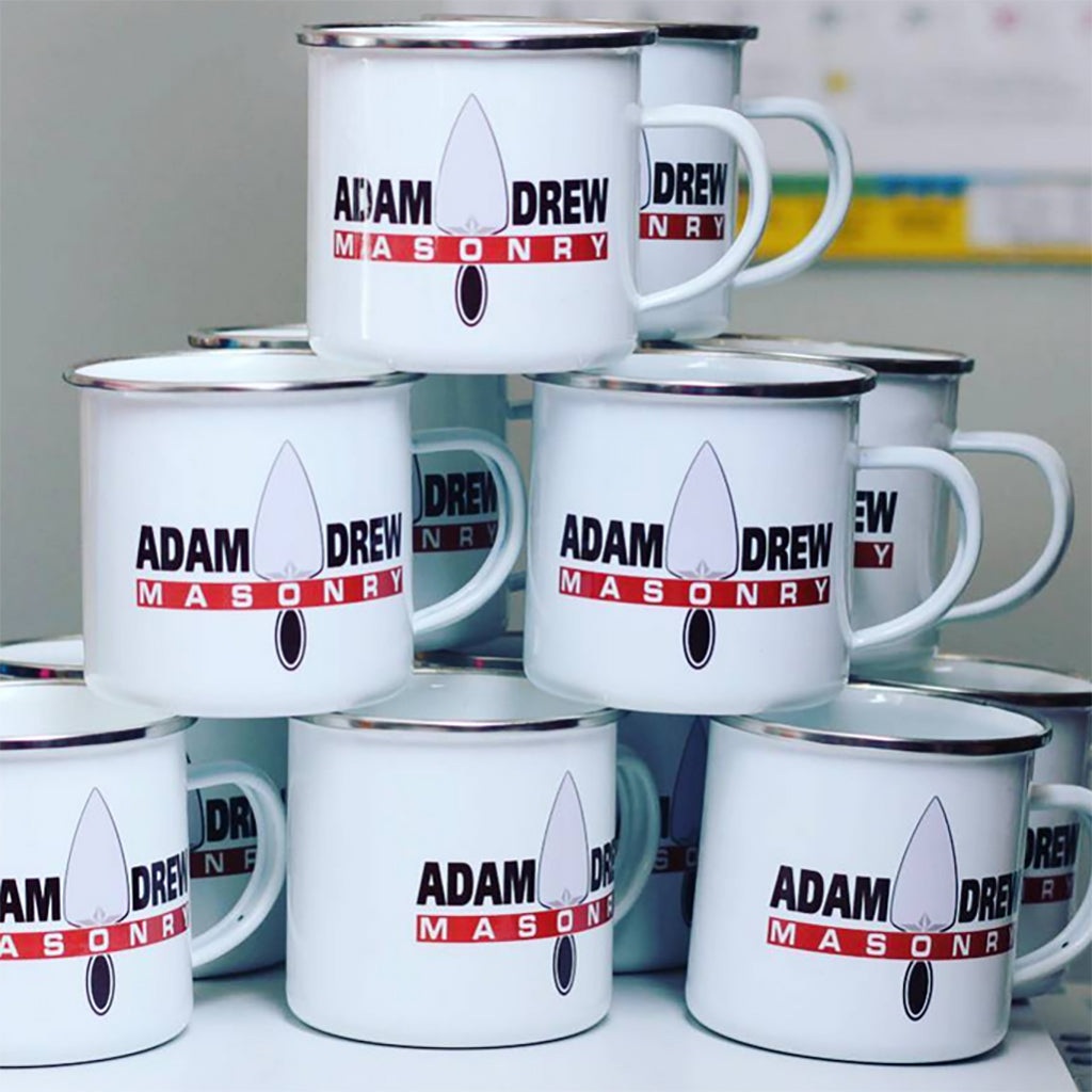 White mugs with 'Adam Drew Masonry' branding on a white surface.